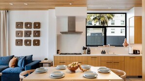Een moderne keuken met houten kasten, een eettafel gedekt met borden en een schaal brood, en een blauwe bank in de woonkamer.