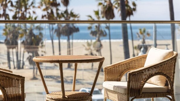 Een balkon met rieten meubilair met uitzicht op een strand met palmbomen en de oceaan.