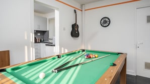 Een pooltafel met ballen en stokken, een klok aan de muur, en een gitaar erboven.