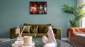 Een woonkamer met een groene bank, een glazen salontafel met decoratieve objecten en een schilderij aan de muur.