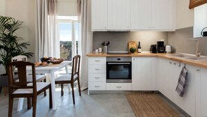 Een moderne keuken met witte kasten, een houten aanrecht, een inbouwoven en een eethoek met een tafel en stoelen.