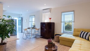 A modern living room with a yellow sofa, a dark cabinet, a dining area with a table and chairs, and a large potted plant.