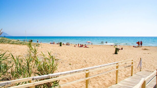 A sandy beach with a wooden boardwalk leading to the water.