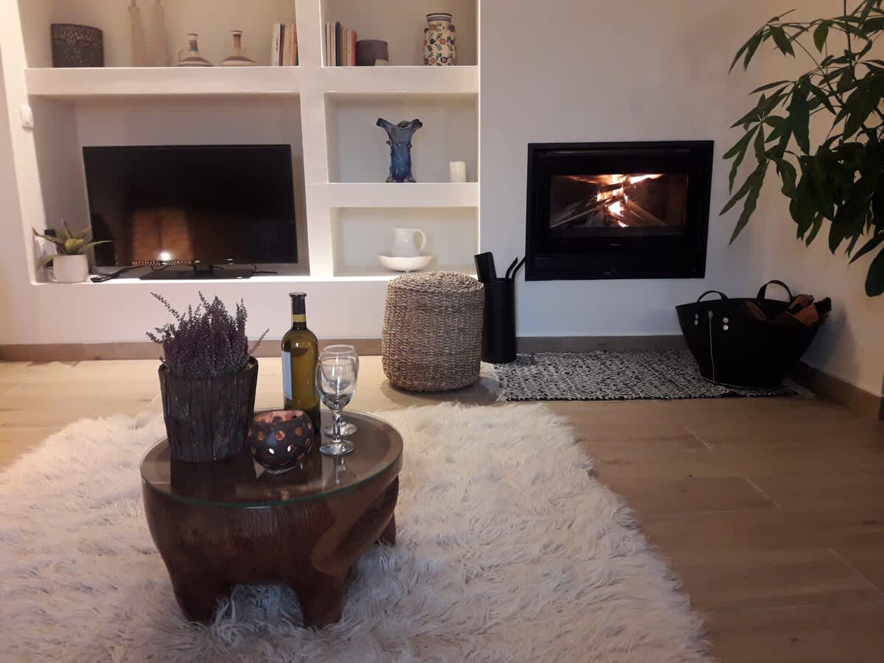 A living room with a fireplace, a glass coffee table, and a white fluffy rug.