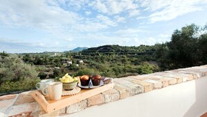 A terrace with a tray of food and drinks, overlooking a scenic landscape with hills and trees.