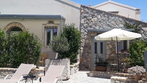 Un bâtiment à la façade en pierre, un patio couvert avec des fauteuils et un ciel d’un bleu éclatant.
