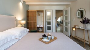 A hotel room with a bed, a bedside table with a lamp, a tray with toiletries, a mirror, and a view of the hallway.