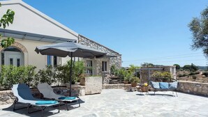 A stone building with a patio area featuring lounge chairs and a table with umbrellas.