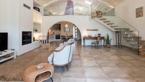 A spacious living area with a high ceiling, a staircase, and a kitchen in the background.