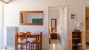 A compact living space with a dining area, a mirror, a radiator, and a bookshelf. - Comfy Beach Flat 10min to the City Center (Kalamata)