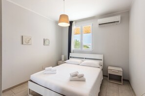 A modern bedroom with a bed, bedside tables, a hanging light, and an air conditioning unit.