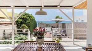 A covered patio with a wooden table, a potted plant, and a view of the sea.