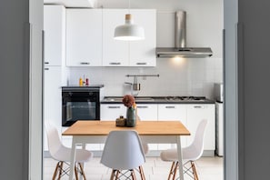 A modern kitchen with white cabinets, a wooden table, and white chairs.