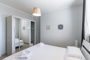 Une chambre d’hôtel moderne équipée d’un lit, d’une armoire, d’un miroir et d’un luminaire au plafond.