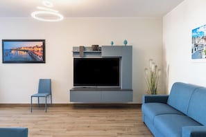 Un salon moderne avec un téléviseur à écran plat, un canapé bleu, un fauteuil et un meuble de rangement fixé au mur.