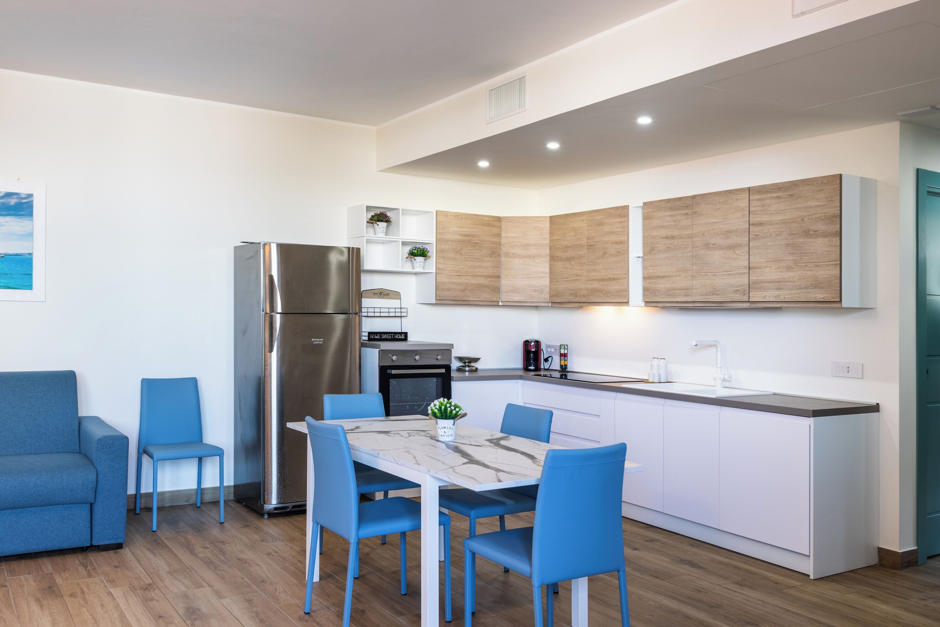 Une cuisine moderne dotée d’un îlot central, de meubles encastrés et d’un coin salon avec des chaises bleues.
