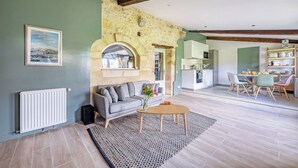 Un salón espacioso con pared de piedra, un sofá gris, una mesa de centro de madera y vistas a la cocina.