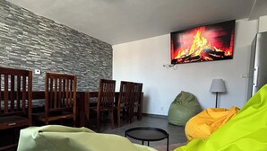 A living room with a stone wall, wooden furniture, a round ceiling light, a fire image on the wall, and a green bean bag chair.