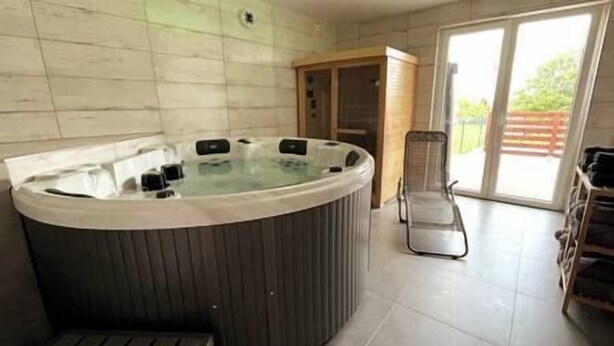 A hot tub in a room with a wooden bench, a chair, and a sliding glass door leading outside.