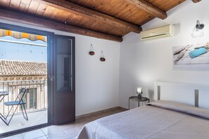 Une chambre avec un lit, un appareil de climatisation, une petite table avec une lampe et un balcon avec une chaise.