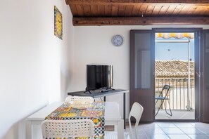 A room with a table, chairs, a TV, a clock, and a balcony door.