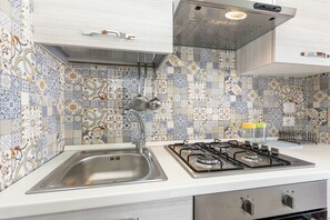 A kitchen with a stainless steel sink, a gas stove, and a patterned backsplash.