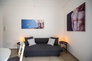Un salon moderne avec un canapé gris, deux tables d’appoint ornées de bougies et deux œuvres d’art accrochées au mur.