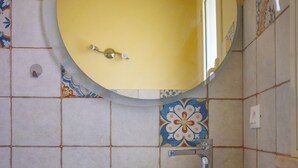 Ein Badezimmer mit rundem Spiegel, Waschbecken in Weiß und gefliesten Wänden.