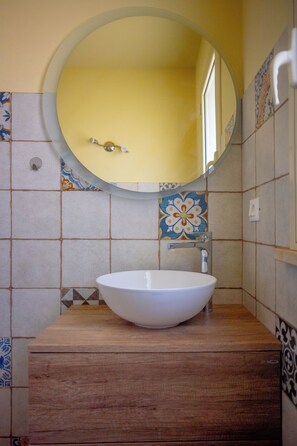 A bathroom with a round mirror, a white sink, and tiled walls.