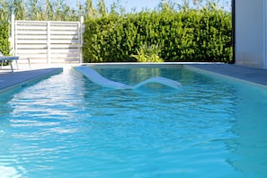 A swimming pool with clear water, a white deck, and a hedge in the background.