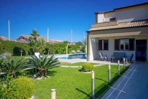 A residential property with a swimming pool, patio furniture, and lush greenery.