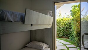 Ein Schlafraum mit Etagenbetten und Blick auf einen Garten durch eine Glastür.