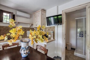 Une cuisine avec une table à manger, un vase rempli de feuilles d’automne, un téléviseur fixé au mur et un espace douche.