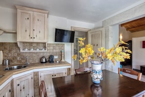 A kitchen with wooden cabinets, a built-in sink, a flat-screen TV, and a vase with yellow flowers on the island. - Relais Casa Bonivini - Scirocco (Noto)
