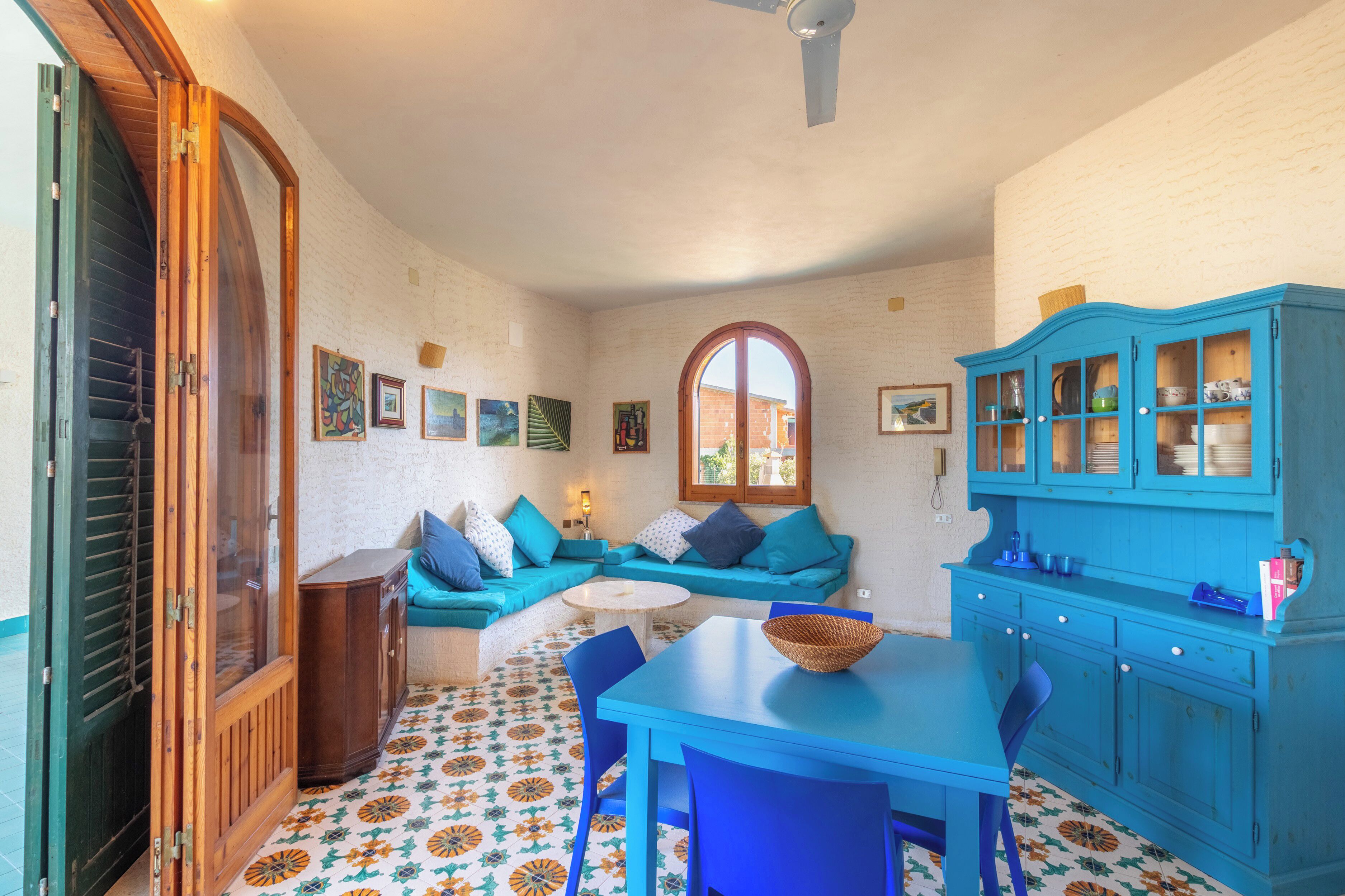 Una stanza con un tavolo blu, sedie, un divano, un armadio e un pavimento decorato.