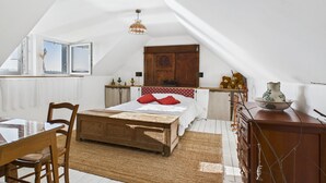 Ein Schlafzimmer mit schrägen Wänden, einem hölzernen Bett, einem Holzschrank, einem Esstisch mit Stühlen und einem Fenster mit Aussicht.