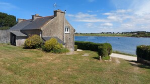 Ein Haus mit Steinaußenwand, einem kleinen Garten und Blick auf einen ruhigen See mit Booten.