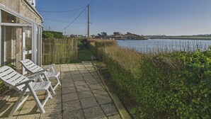 Eine Terrasse mit weißen Stühlen und Steinboden, mit Blick auf ein Gewässer und eine entfernte Küste.