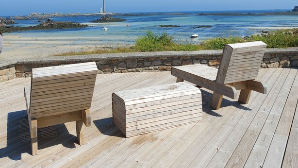 Un muelle de madera con dos sillas orientadas hacia la vista costera.