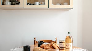Una mesa de madera con platos, una taza negra, una botella de JUS de Vourtière y una cesta de cruasanes.