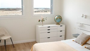 Un dormitorio con cama, escritorio, un globo terráqueo y vista a la playa.