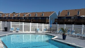 A clear swimming pool with lounge chairs and a white fence.