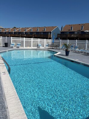 A clear swimming pool with lounge chairs and a white fence.