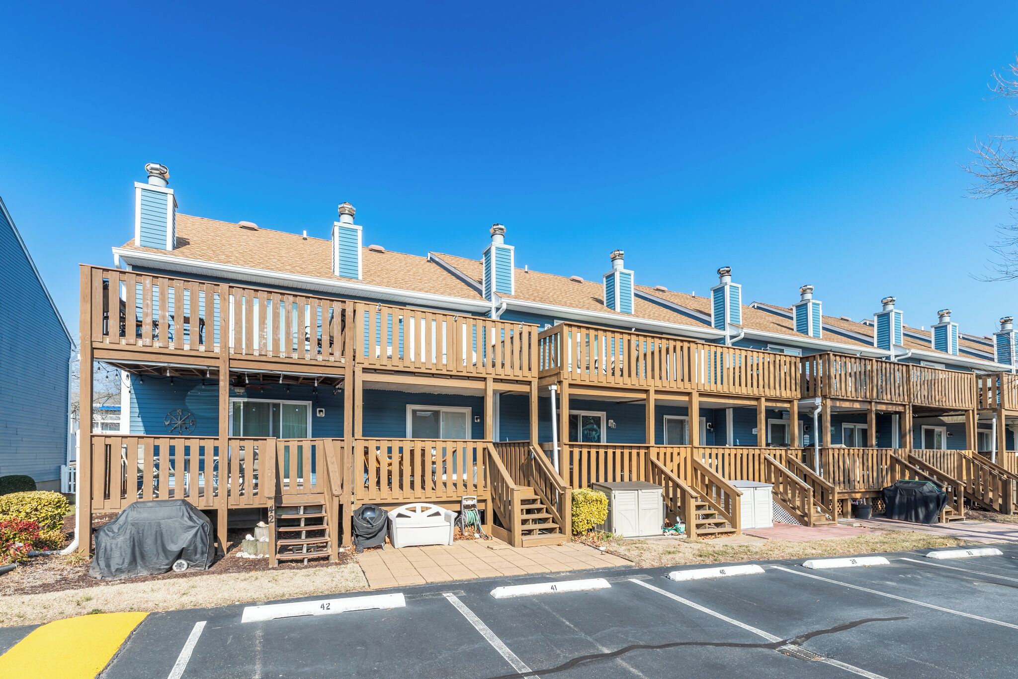 A row of wooden cabins with balconies, a covered outdoor seating area, and a parking lot.