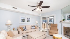 A living room with a beige sofa, a white ottoman, a wicker chair, and a ceiling fan.