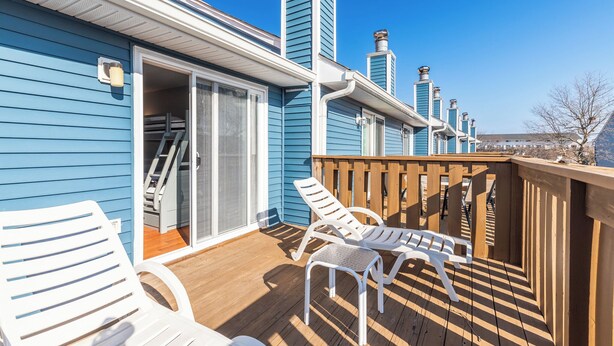 A blue building with a wooden deck, two white lounge chairs, and a wooden railing.