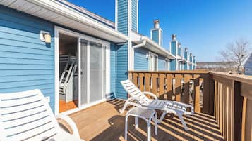 A blue building with a wooden deck, two white lounge chairs, and a wooden railing.