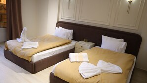 Dos camas dobles con cabeceros marrones y ropa de cama blanca, una mesita de noche con lámpara y una ventana con cortinas.