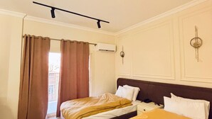Habitación de hotel con dos camas, ventilador de techo, equipo de aire acondicionado y vista al balcón exterior.
