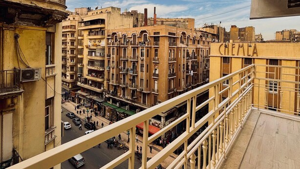 Un balcón con vista a una zona urbana densamente poblada, con edificios de varios pisos y balcones, bajo un cielo despejado.